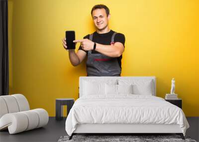 Young man worker with tools belt pointed on phone isolated on yellow background Wall mural